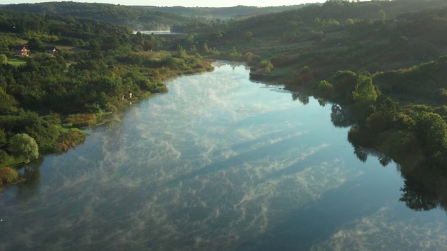 清晨的薄雾浮在平静的水面上，湖面上是丘陵的风景。视频素材