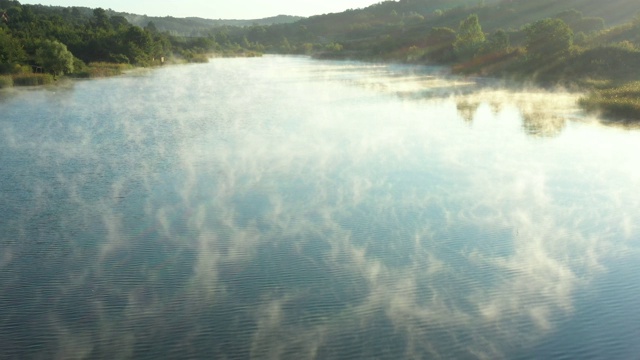 清晨的薄雾浮在平静的水面上，湖面上是丘陵的风景。视频素材