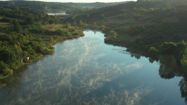 清晨的薄雾浮在平静的水面上，湖面上是丘陵的风景。视频素材