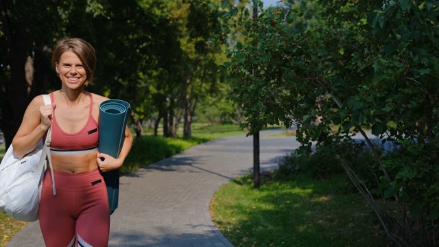 在操场上晨练后穿着运动服的女人。一个拿着健身垫练习瑜伽的女人。视频素材