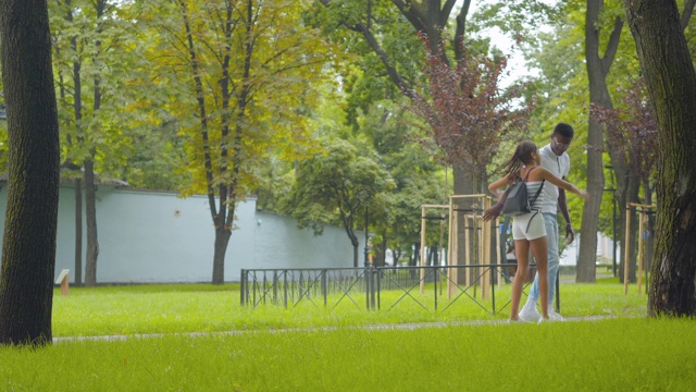 宽镜头的快乐的非洲裔美国女孩跑到微笑的男人在阳光明媚的一天。快乐的哥哥拥抱姐姐和兄弟姐妹离开。欢乐的一家人在户外夏日公园散步。视频素材