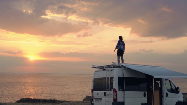 日落时分，一个女人在海边露营车的屋顶上跳舞视频素材