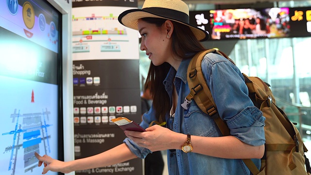 美丽的亚洲女人穿着旅游服装，正在查询航班时刻表。出国旅行可以用于代表独自旅行的概念作品中。视频素材