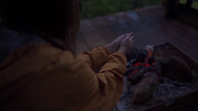 慢镜头剪影后视图的女人在黄色夹克温暖她的手篝火在晚上的农舍露台。年轻女子喜欢户外生活方式和徒步旅行。秋季旅游度假和露营概念。视频素材