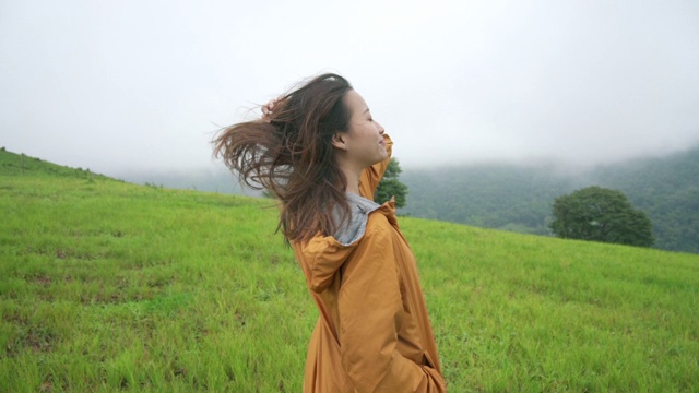 慢动作的微笑年轻女子在黄色夹克徒步登山在假期的山路。美丽的女孩感到自由，享受走在绿色草甸山上。户外生活方式活动与自然概念视频素材