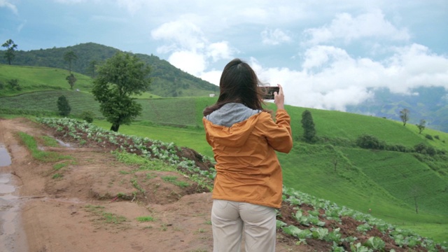 风儿吹过山岭，身穿黄夹克的年轻女子站在山顶的慢镜头后视图。美丽的女孩感到自由，享受徒步在绿色的草地。户外生活方式和自然旅游理念视频素材