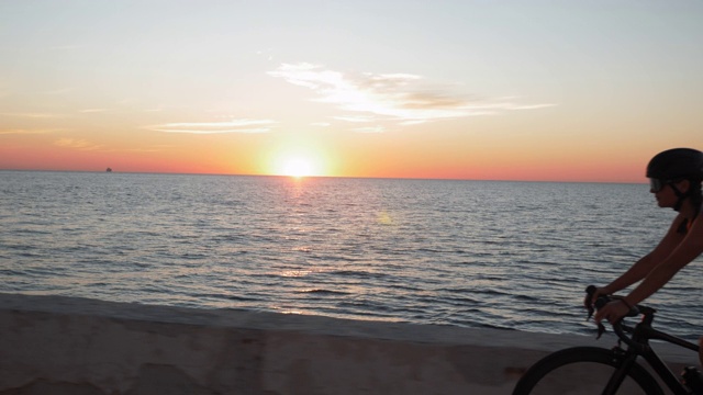 一个女人在夕阳下骑自行车，背景是大海。日出时分，女自行车手穿着休闲装，戴着时髦的眼镜，骑着公路自行车沿着海滨骑行视频素材