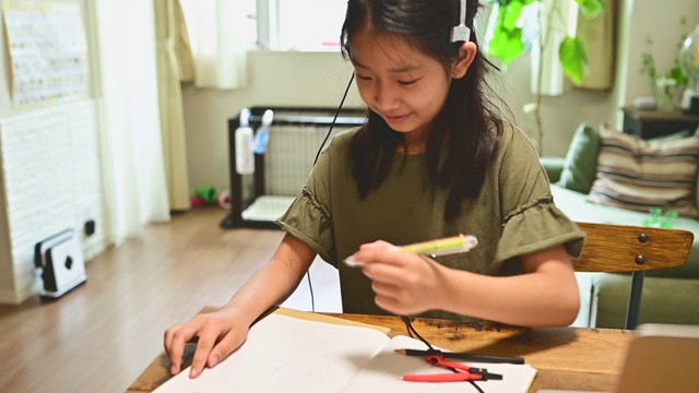 小学女孩学习视频在线课程在家里的客厅。视频素材