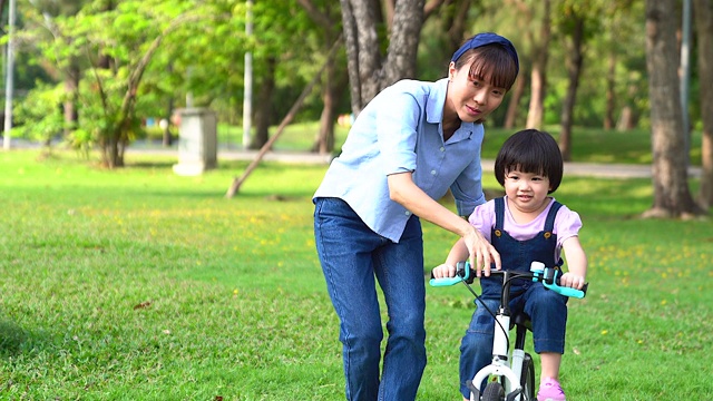 妈妈在一个阳光明媚的公园里教一个骑自行车的小女孩。学龄前儿童在公园里学习骑自行车保持平衡。视频素材