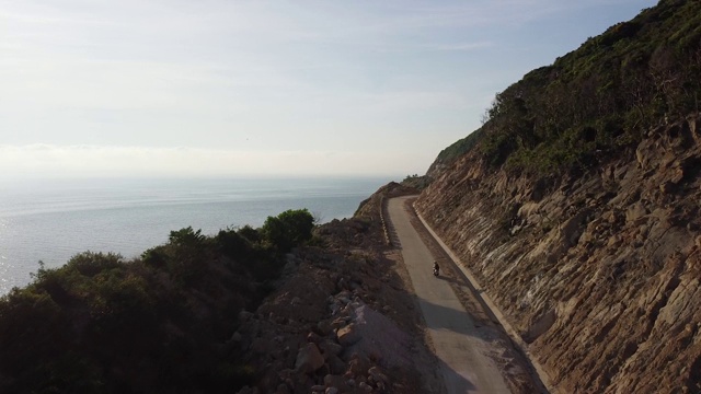 一架无人机在沿海一条弯曲空旷的道路上尾随一名摩托车手。视频素材