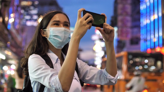 一名女性旅游博主在旅游博客中使用智能手机摄像头夜间行走视频素材