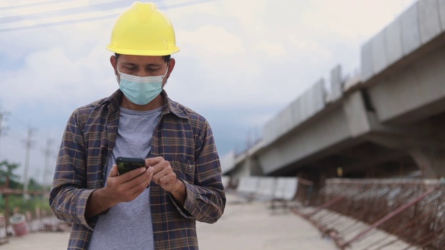 建筑工人在工地上戴着防护口罩并使用智能手机视频素材