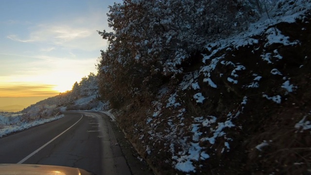 日落时分，在冰雪覆盖的冬日森林里的山路上开车视频素材