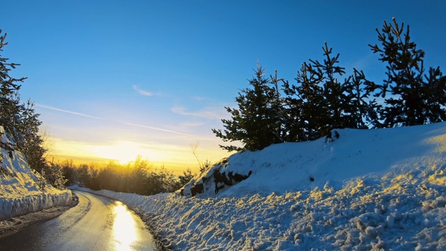 日落时分，在冰雪覆盖的冬日森林里的山路上开车视频素材