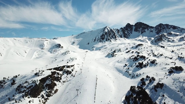 在安道尔的格兰德瓦利拉滑雪胜地沿着滑雪斜坡平稳移动的鸟瞰图。壮丽的雪山和蓝天。冬天的风景视频素材