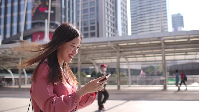 亚洲女商人一边使用智能手机一边行走在城市里视频素材