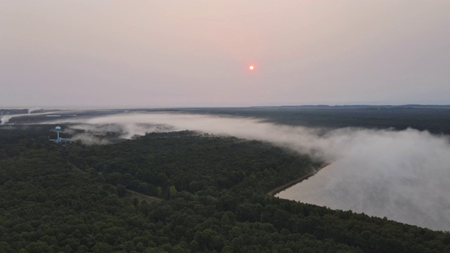 在雾霾的早晨，一架无人机在空中飞过湖面景观和绿色森林景观视频素材