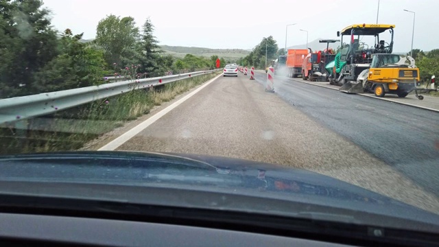 在有雨点打在挡风玻璃上的高速公路上驾驶POV，有交通标志的道路施工限制视频素材