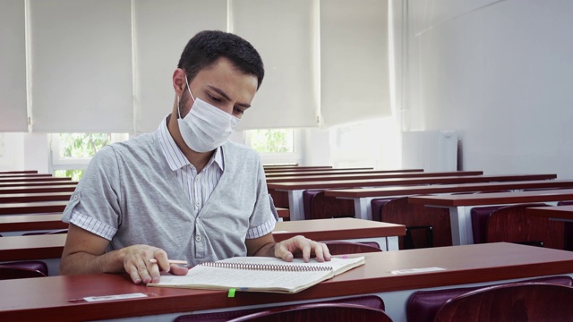 由于冠状病毒感染，一名年轻男子戴着口罩，独自在一所大学的空讲堂学习视频素材