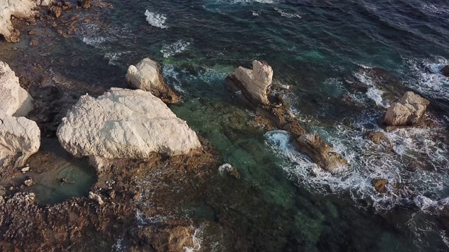 鸟瞰塞浦路斯的海岸线，海浪拍打着岩石，一名年轻女子在天然泳池中游泳视频下载