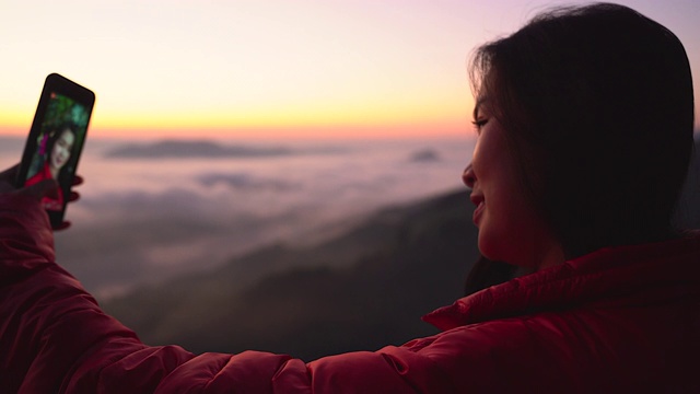 在有阳光和雾的山上拍摄风景的年轻女子的剪影。带着相机独自旅行的背包客。假日旅游和度假概念。视频素材