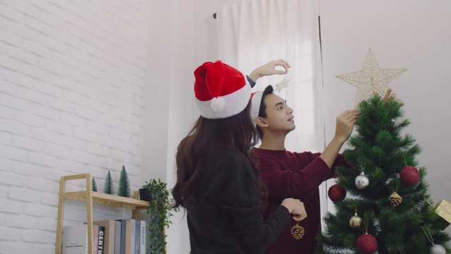 年轻的亚洲夫妇装饰圣诞树在圣诞节和快乐的新年节日在家里的背景。圣诞节庆祝情人的概念。4 k慢动作。视频素材