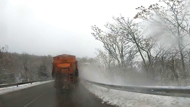 后视镜扫雪机服务卡车和撒盐砂砾路面，以防止结冰在暴风雪的冬天的日子，缓慢的动作视频素材