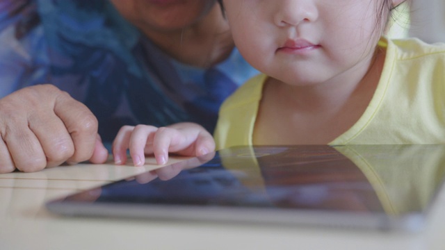 手持POV拍摄奶奶和孙子在家客厅看数字平板电脑。快乐的爷爷和孙女一起看电子屏幕，在家里放松。可爱的小女孩用手指触摸屏幕。视频素材