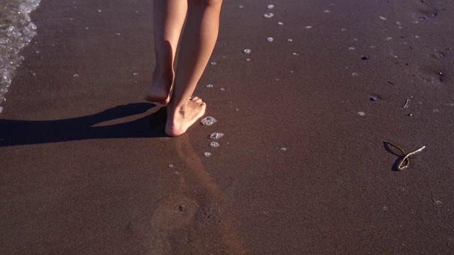 年轻女子的脚走在潮湿的沙滩附近的海浪边缘视频素材