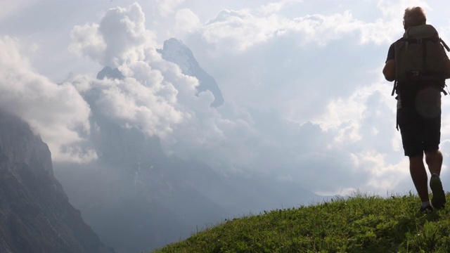 一名男性徒步旅行者在草甸斜坡上停下来，眺望群山视频素材