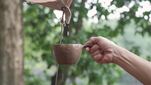 用手把帐篷或防水布里的雨水倒入室外的杯子里。视频素材