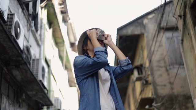 美丽的年轻女性亚洲旅行者戴着复古软呢帽用胶片相机在泰国曼谷的一条小街上拍照。视频素材