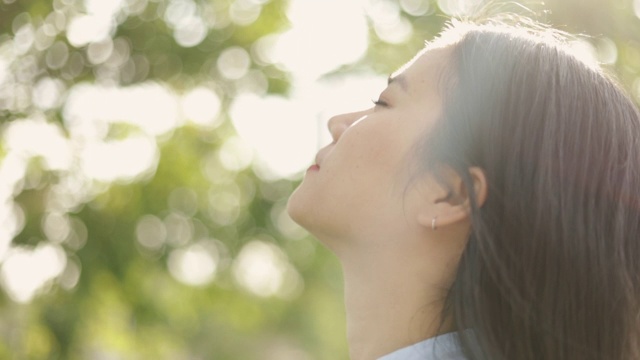 年轻的亚洲女人的近距离肖像放松享受和平的日落，抬头呼气新鲜空气放松在一个美丽的夏季日落公园。视频素材