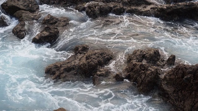 蓝绿色的海浪撞击着海岸附近的火山岩。视频素材