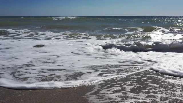 从上面看海岸线。航拍美丽的波涛汹涌的大海和泡沫的海浪。柔和的波浪在沙滩边拍打着并产生泡沫。鸟瞰画面视频素材