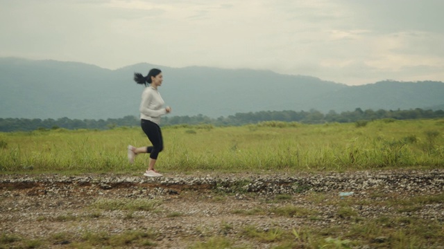 亚洲女性在乡村公路上跑步，山景美丽的早晨。视频素材