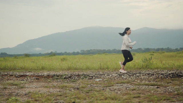 美丽的亚洲女人在乡村公路上跑步，山景美丽的早晨。视频素材