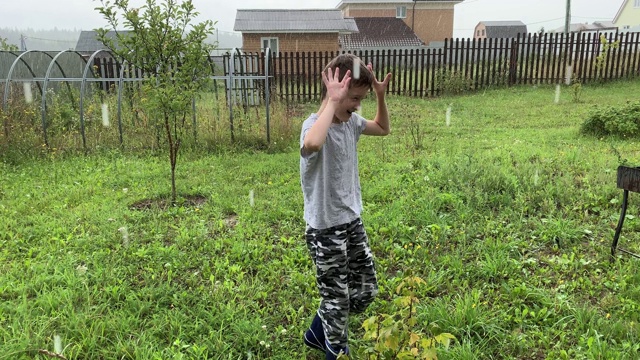 一个快乐的微笑的男孩站在倾盆大雨下，捕捉雨滴，倾盆大雨和恶劣的天气视频素材