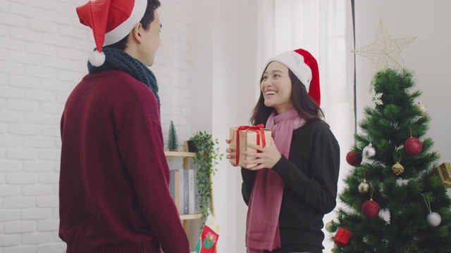 年轻的亚洲夫妇给对方一个礼物盒在圣诞节和新年期间在家里的背景与圣诞树装饰节日节日。圣诞节庆祝活动的概念。4 k慢动作。视频素材