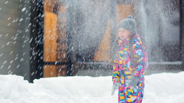 梳着辫子的漂亮女孩穿着暖和的衣服在院子里玩雪球视频素材