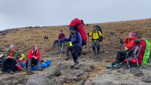 两个背着大背包拿着登山杖的徒步旅行者经过一群露营者。视频素材