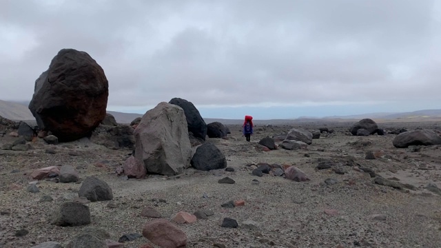 一个孤独的旅行者背着一个巨大的背包沿着高山高原走过巨石。视频素材