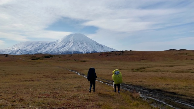 两名背着大背包、拄着拐杖的游客正沿着冻土带上的小径行走。视频素材