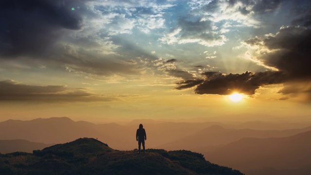 一个人站在山顶上，映衬着灿烂的夕阳。时间流逝视频素材