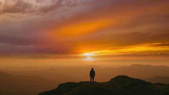 一个人站在山顶上，背景是明亮的夕阳视频素材