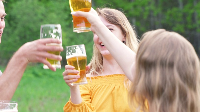 朋友们在夏天的户外聚会上喝啤酒。年轻女子敬酒，喝啤酒。在假期里玩得开心的女孩。快乐的朋友休闲活动野餐度假。酒精饮料。视频素材