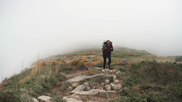 一个背着大背包的女人爬上了山坡视频素材