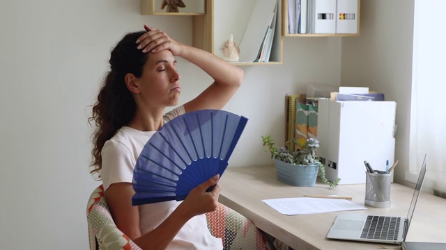 女人挥动着手持的蓝色扇子冷却自己感到过热视频素材