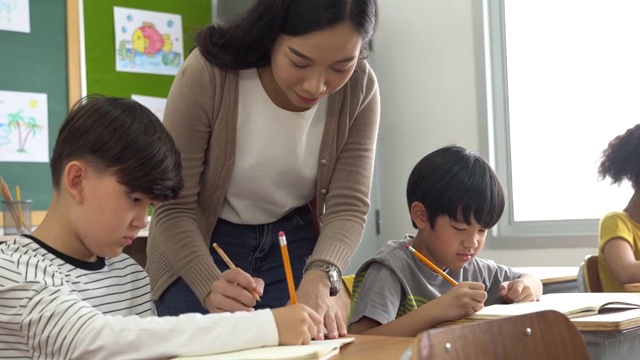 亚洲学校的老师在课堂上帮助学生。年轻女子在学校工作，帮助男孩写作，教育，支持和关心视频购买