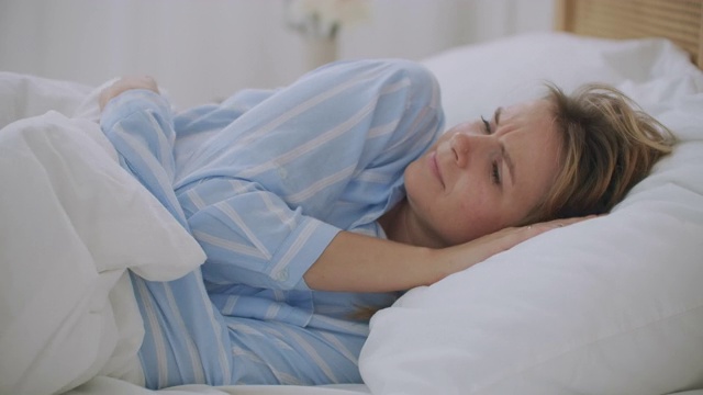 年轻女子躺在床上与格子颤抖冻感觉寒冷在家里没有中央供暖问题在寒冷的季节，生病生病的女孩包裹在毯子有发烧流感的症状视频素材